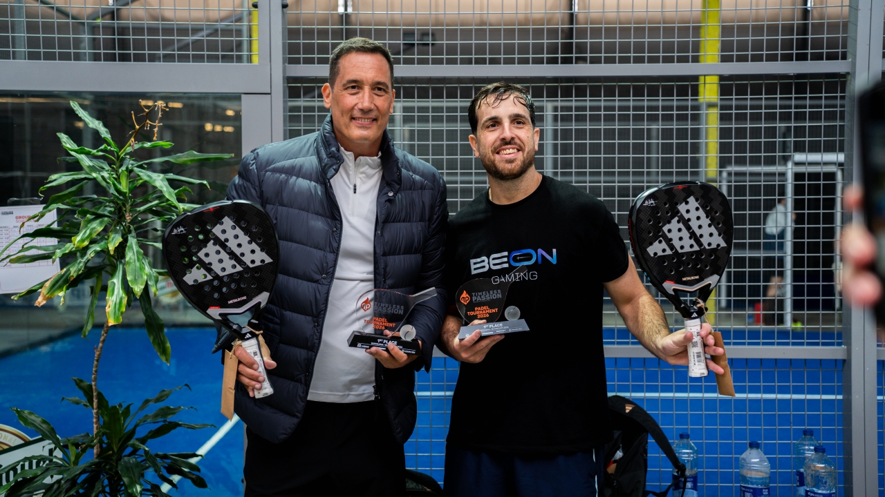 Dois vencedores do Torneio de Pádel Timeless Passion posam com seus troféus e raquetes na quadra indoor após a final